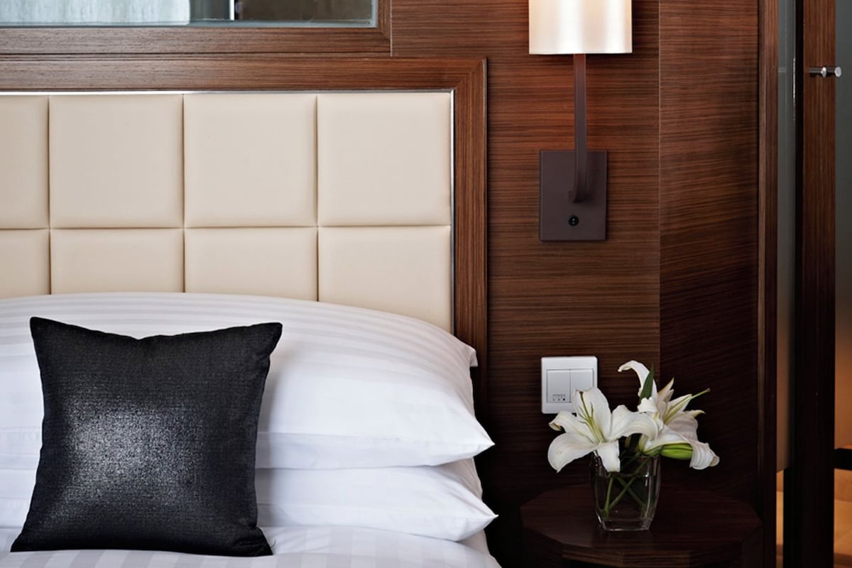 Una habitación de hotel con una cama, una mesita de noche con una lámpara y un jarrón con flores.