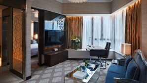 Habitación de hotel moderna con una tele grande, un sofá, una mesita de centro y un escritorio con una silla.