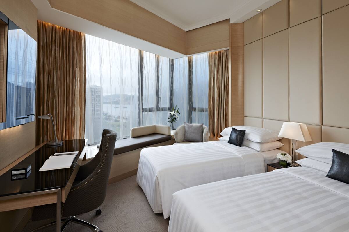 Een hotelkamer met twee bedden, een bureau, een stoel en een groot raam met gordijnen.