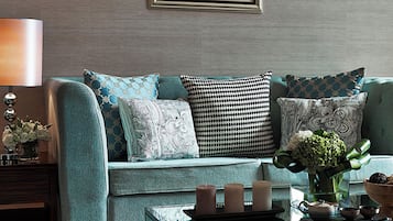 A modern living room with a teal sofa, patterned cushions, a framed artwork, and a coffee table with decorative items.