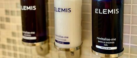Three Elemis bath products on a tiled wall.
