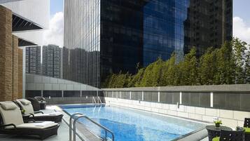 An indoor swimming pool with lounge chairs and a view of tall buildings.