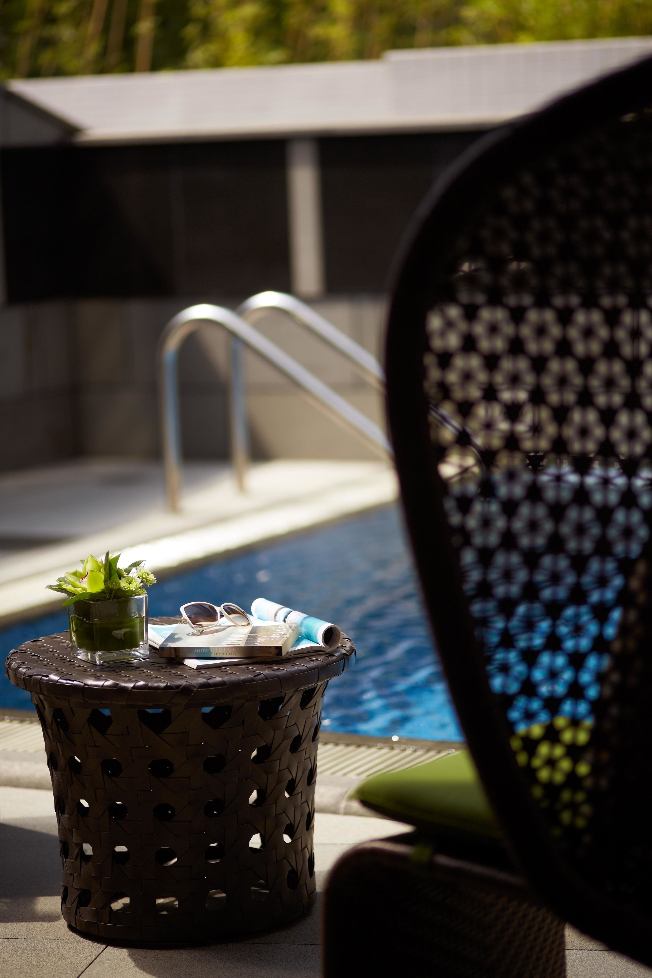 A poolside area with a small table holding a plant, sunglasses, and a towel.