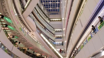 A multi-level shopping mall with escalators connecting different floors, glass ceilings, and various stores.