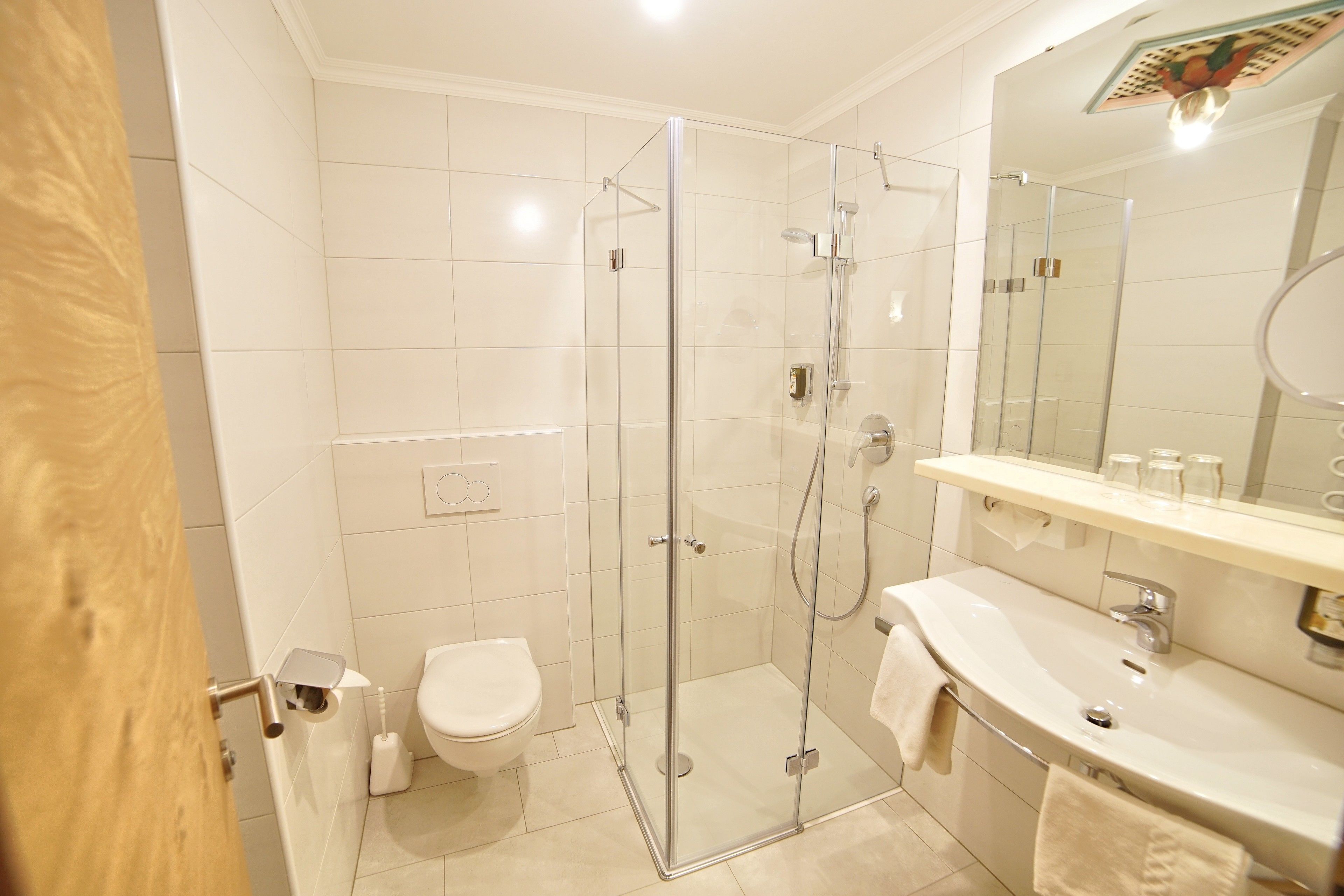 Een moderne badkamer met een douche in een glazen cabine, een toilet en een wastafel met spiegel erboven.