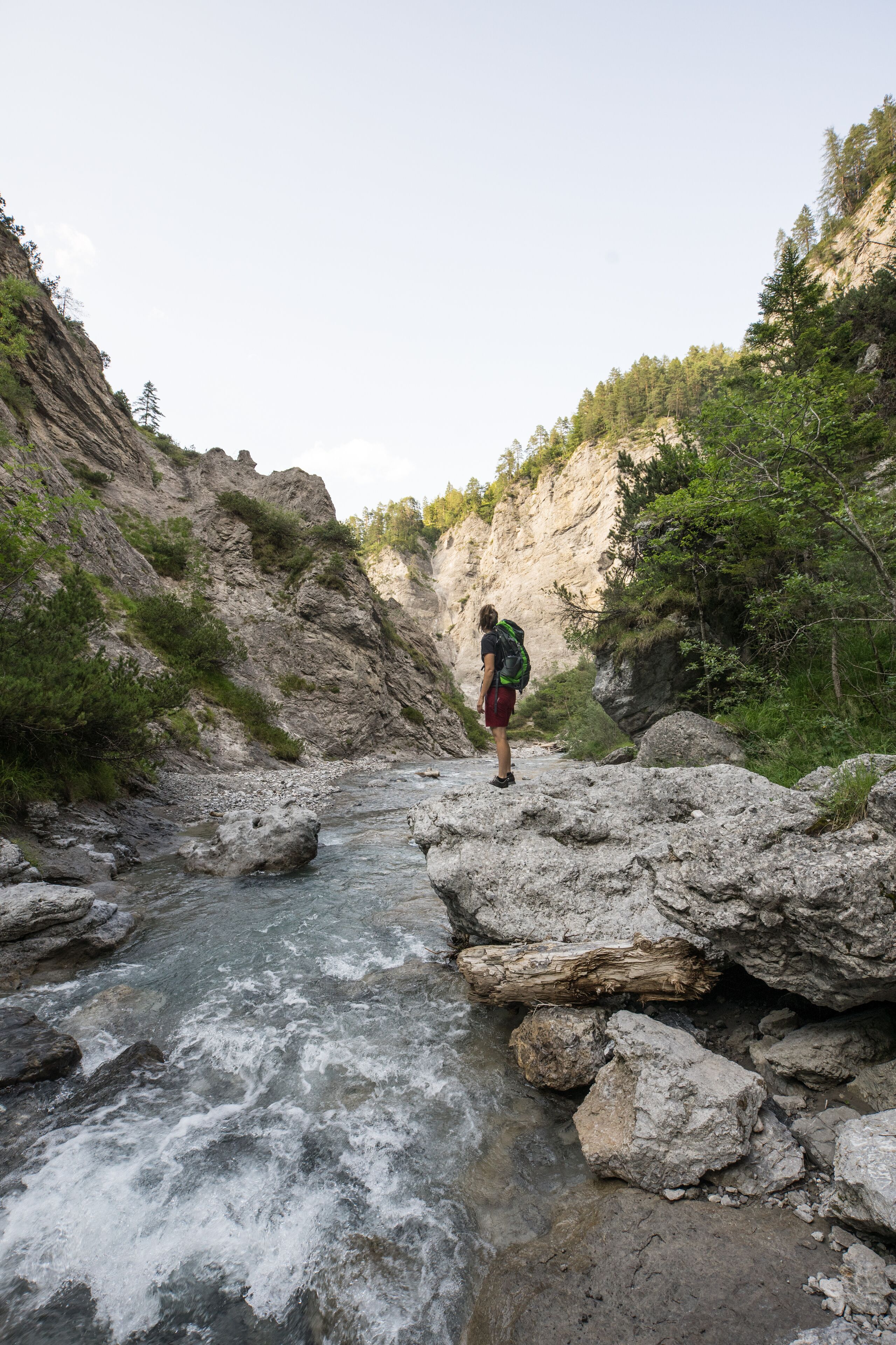 A person standing on rocks by a flowing river in a mountainous area.