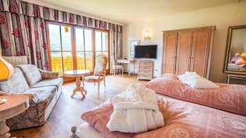 Habitación de hotel con sofá, dos camas con toallas, escritorio con televisor, silla y armario.