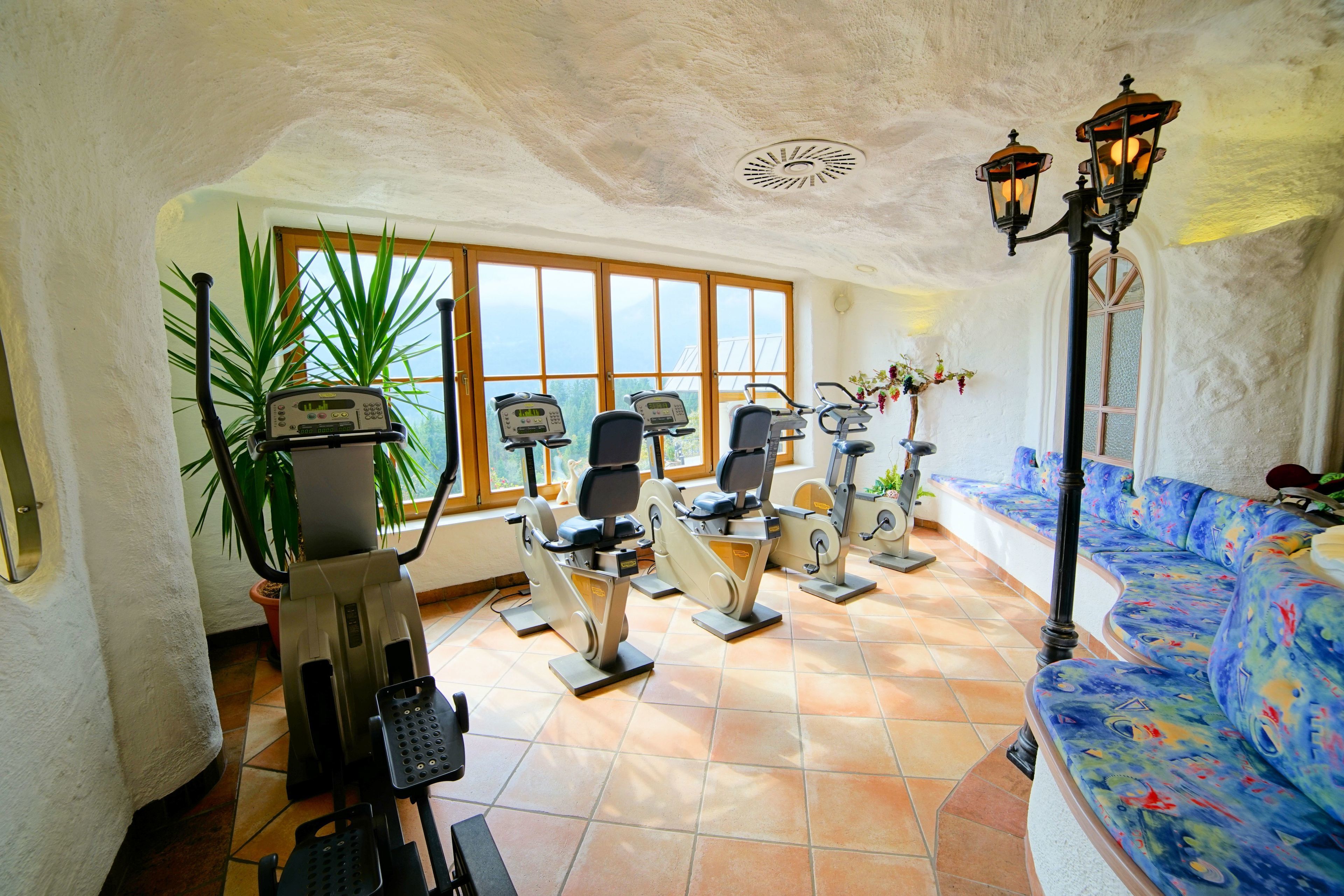 A room with exercise equipment, a large window, and a sofa with a colorful design.