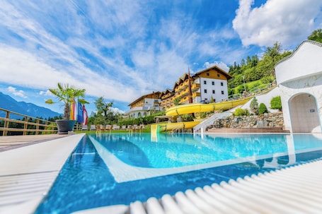 A swimming pool with a yellow water slide, surrounded by buildings with balconies and a mountain backdrop.
