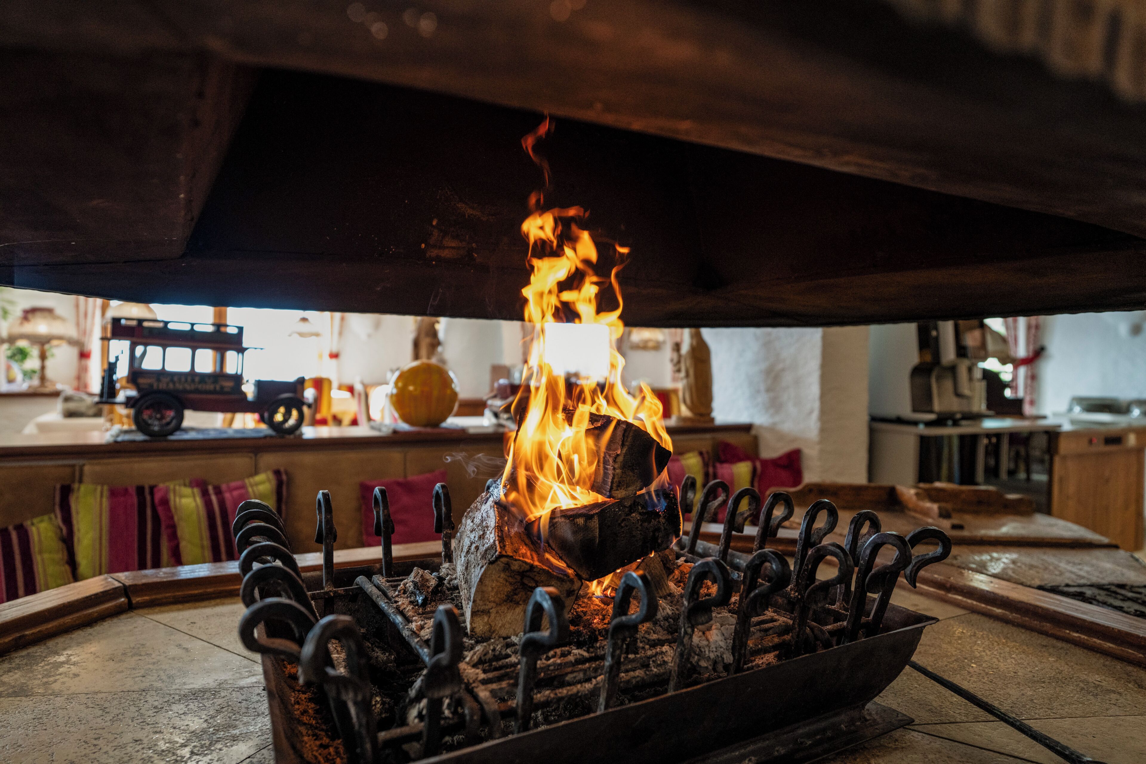 Un fuoco sotto una struttura in legno, probabilmente un tavolo o un bancone, con ganci metallici e una ciotola.