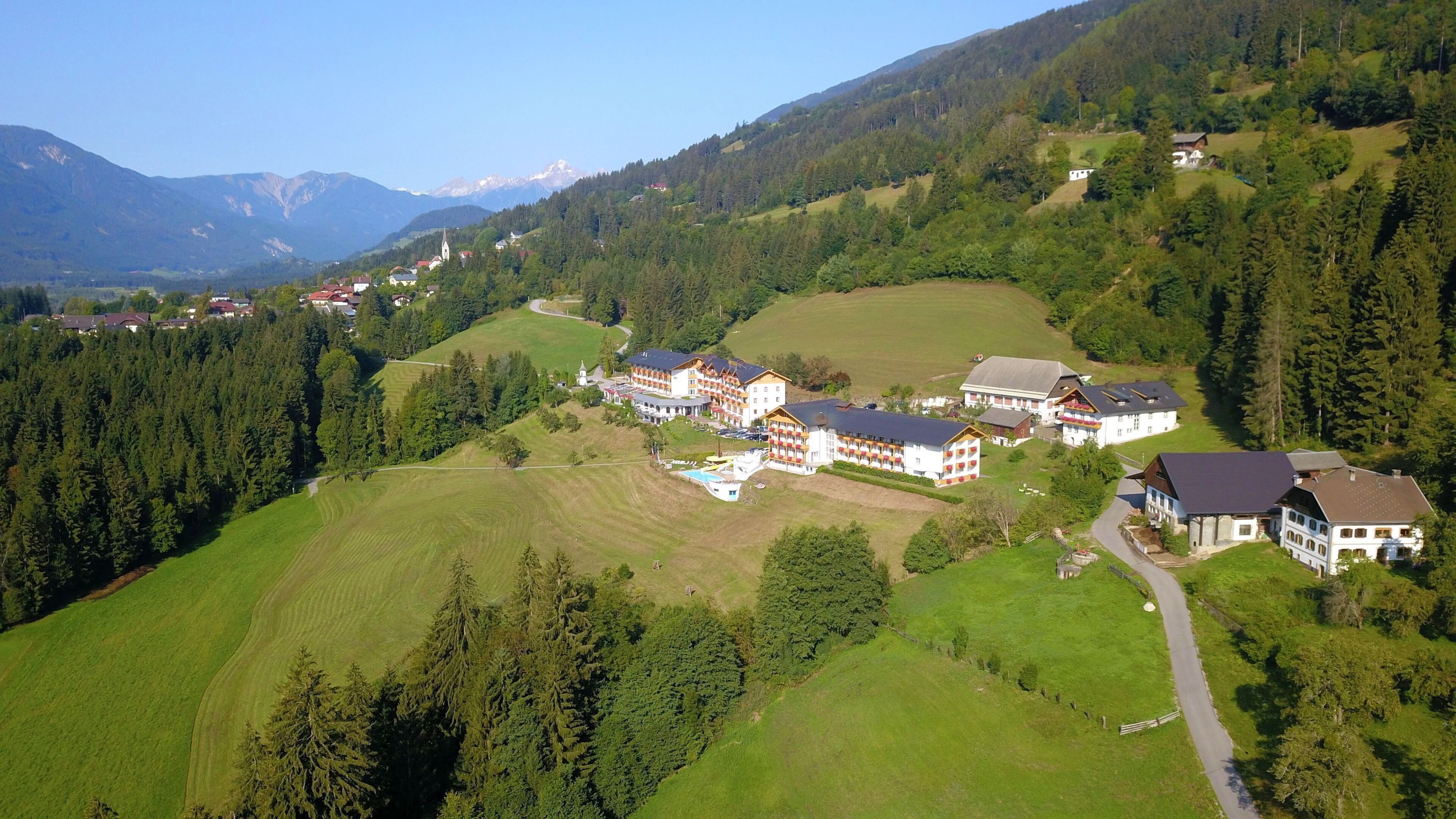 Un complejo turístico de montaña con varias edificaciones de estilo chalet, una piscina e iglesia.
