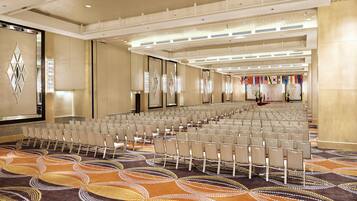 A large conference room with rows of chairs, a patterned carpet, and a stage with flags.