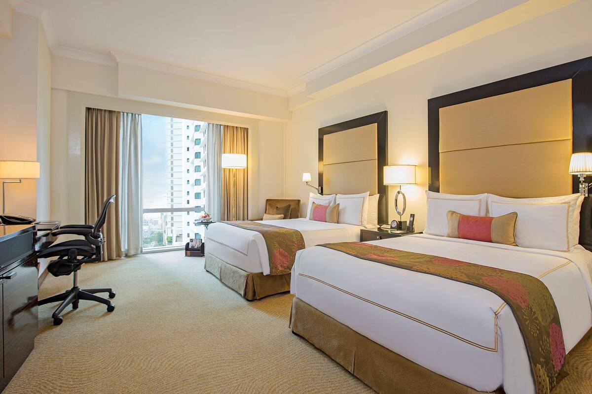 A hotel room with two beds, a desk, and a chair.