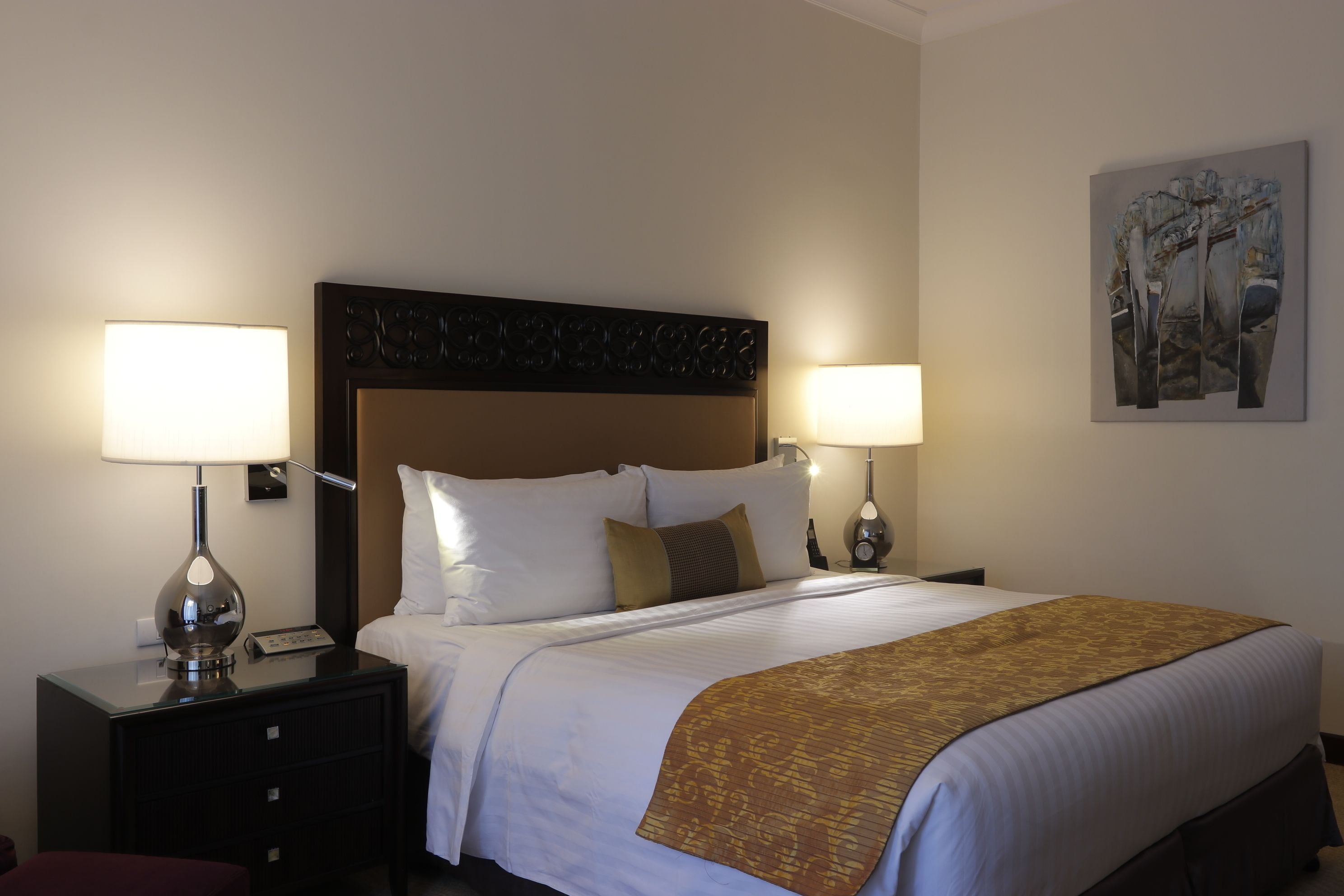 A hotel room with a large bed, two bedside tables with lamps, a headboard, and a wall-mounted artwork.