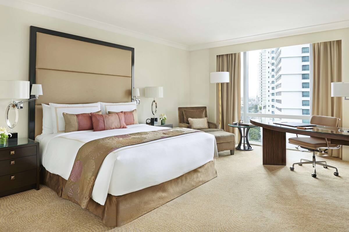 A hotel room with a large bed, a desk, a chair, and a view of the city.