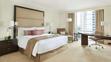 A hotel room with a large bed, a desk, a chair, and a view of the city.