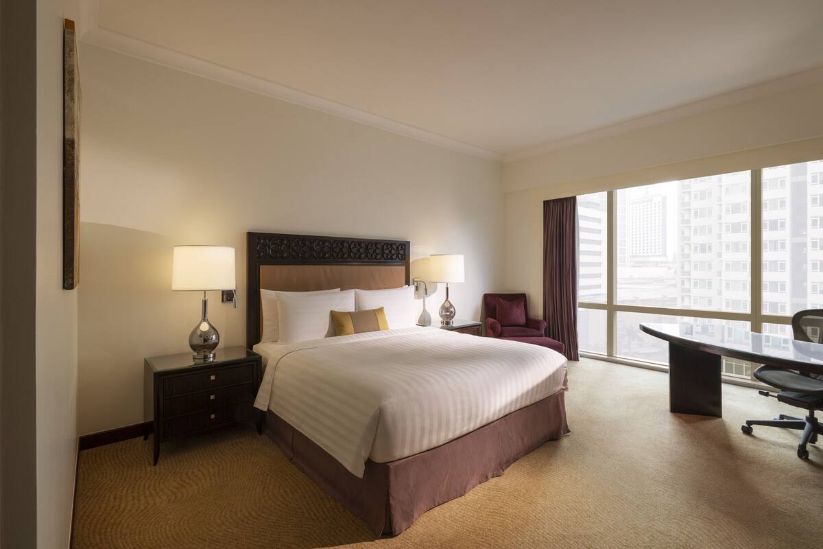 A hotel room with a large bed, two bedside tables with lamps, a desk, and a chair.