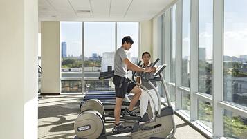 Un gimnasio con equipo de ejercicio, amplias ventanas y vistas a la ciudad.