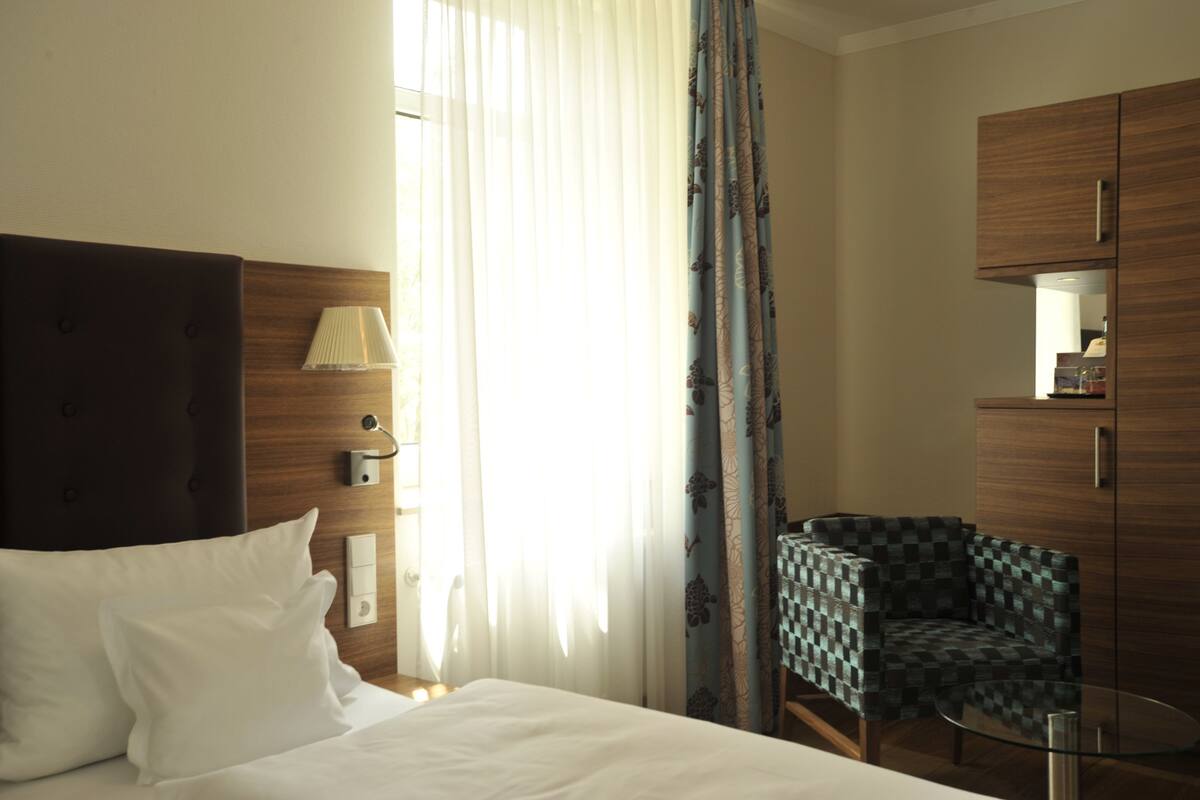 Une chambre d’hôtel avec un lit, une chaise, une petite table et une armoire.