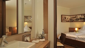 Une chambre d’hôtel dotée d’un grand miroir, d’une coiffeuse en bois, d’un lit avec du linge de lit blanc et d’une œuvre d’art accrochée au mur.