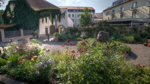 Une cour intérieure avec un bâtiment recouvert de lierre, un mur de pierre et une variété de plantes à fleurs.