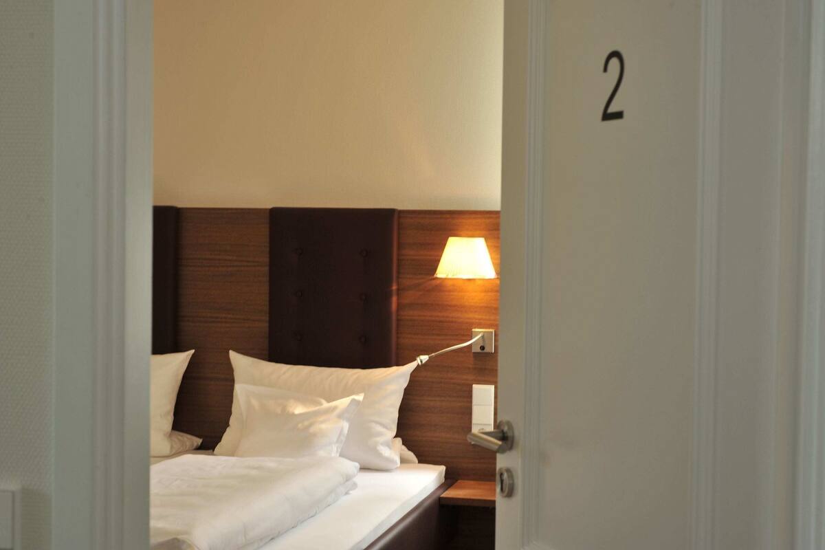 Une chambre d’hôtel avec un lit, une table de chevet, une lampe et une porte portant le numéro 2.
