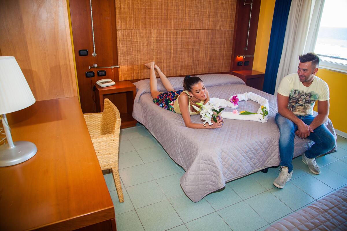 A hotel room with a bed, a bedside table with a lamp, a chair, and a window with curtains.