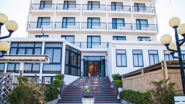A multi-story hotel with a central entrance, a staircase leading to the entrance, and a decorative planter with flowers at the base. - Hotel Park (Chioggia)