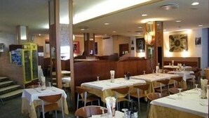 A restaurant with multiple tables and chairs, a counter, and a staircase leading to an upper level. - Hotel Park (Chioggia)
