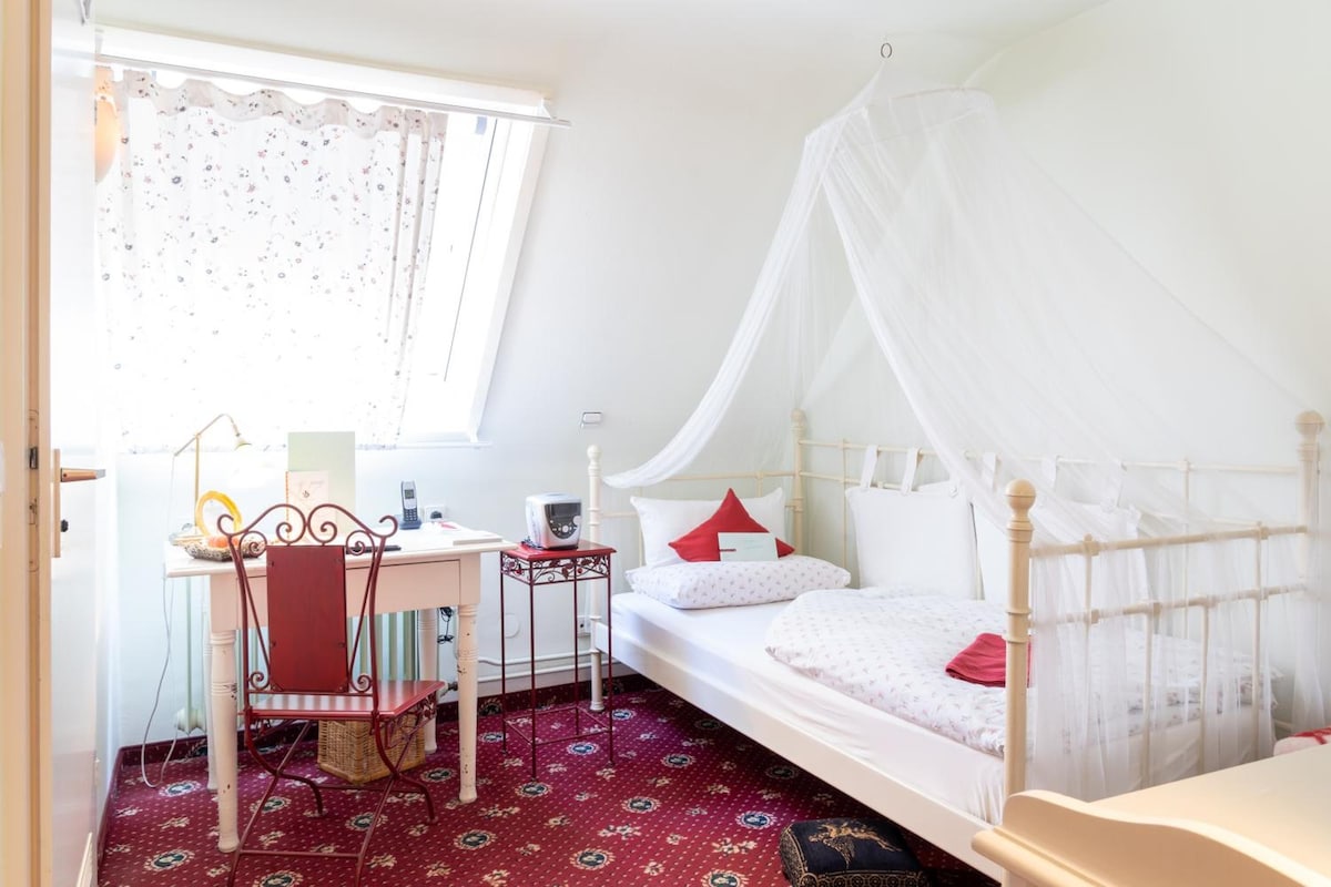 A bedroom with a bed, a desk, a chair, and a window with curtains.