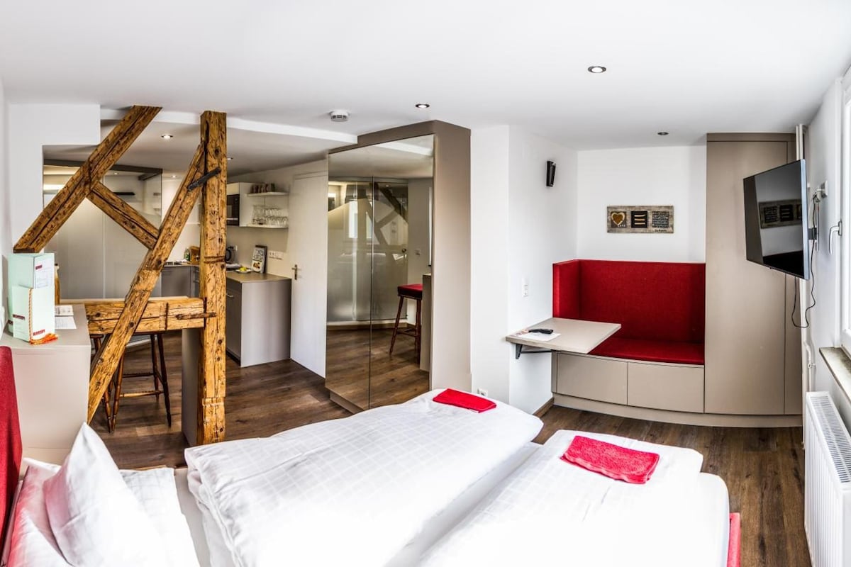 A hotel room with a bed, a red couch, a TV, and a wooden structure.
