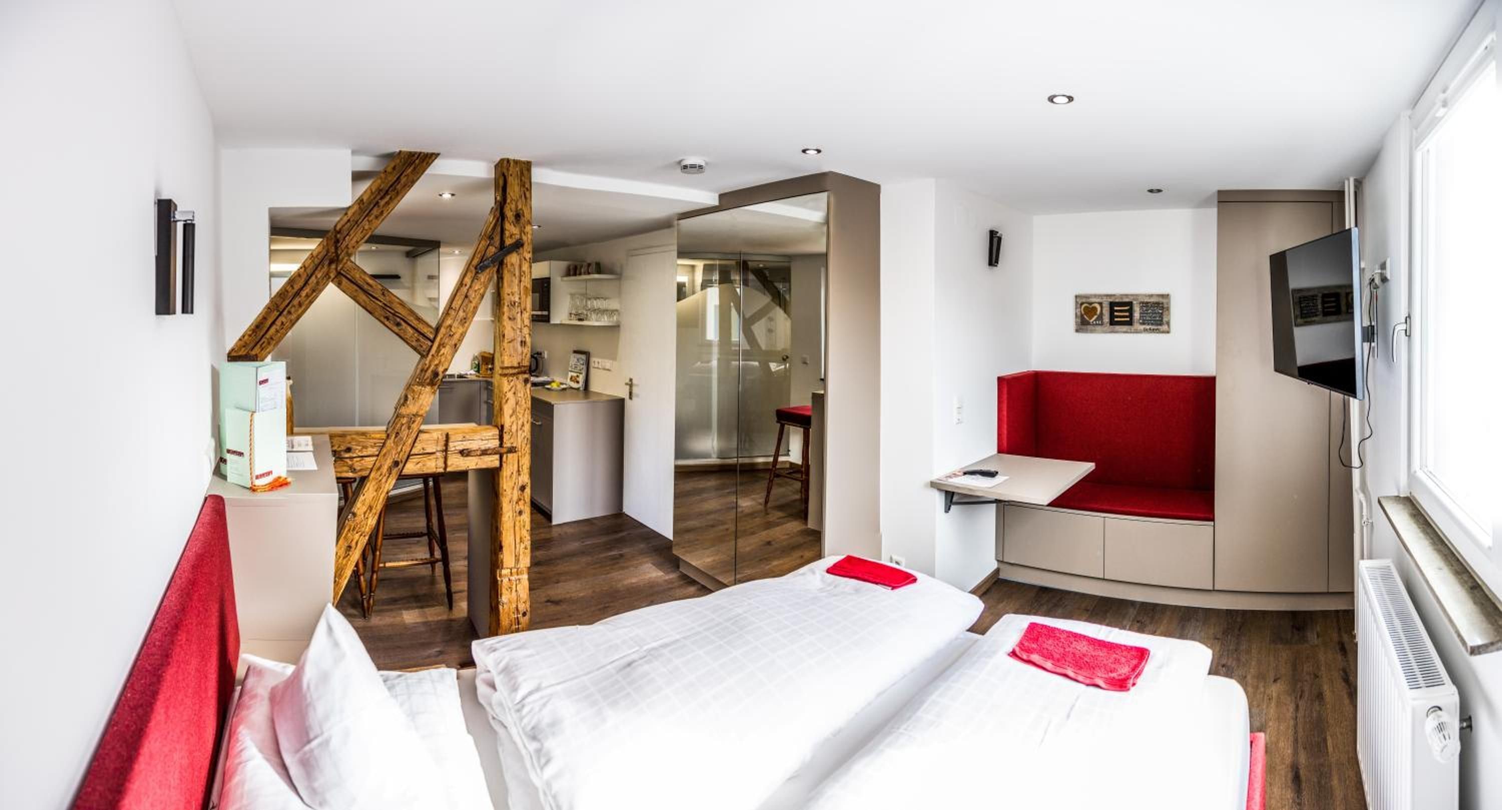 Ein Hotelzimmer mit einem Bett, einer roten Couch, einem Fernseher und einer Holzkonstruktion.
