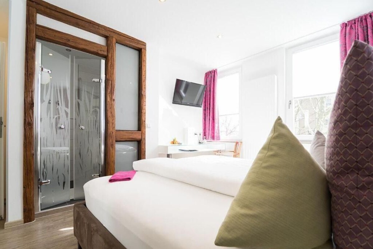 A hotel room with a bed, a television, a desk, and a window with curtains.