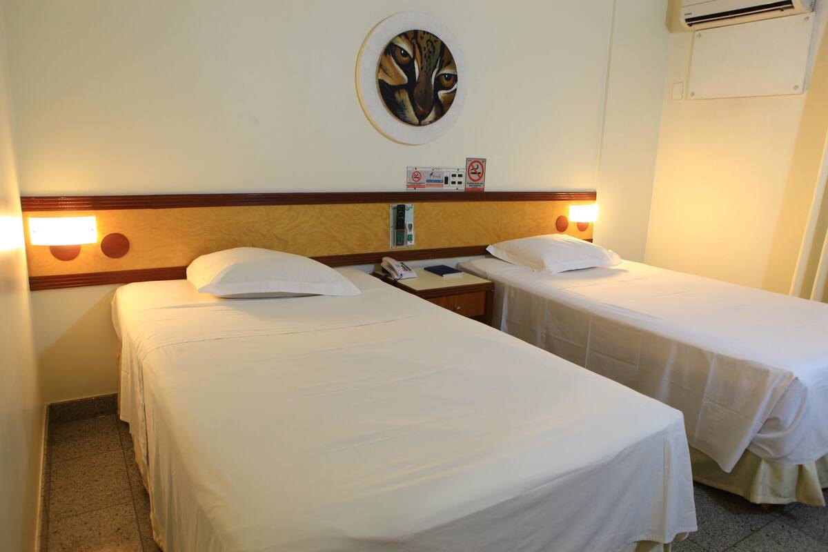 A hotel room with two single beds, a wall-mounted air conditioning unit, and a wall clock.