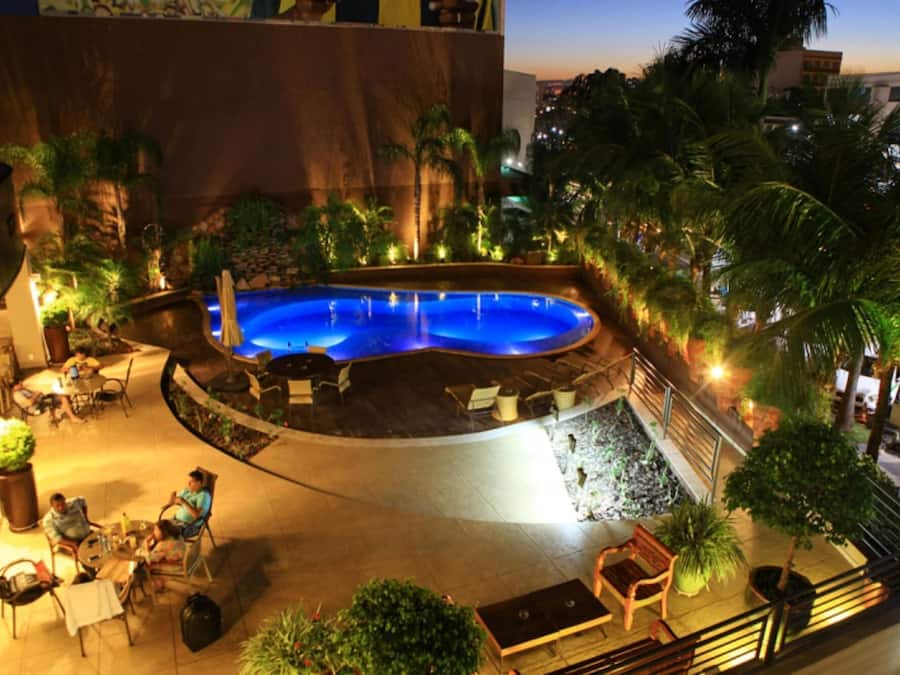 Ein Pool mit gewölbter Kante, umgeben von Sitzgelegenheiten und Palmen.