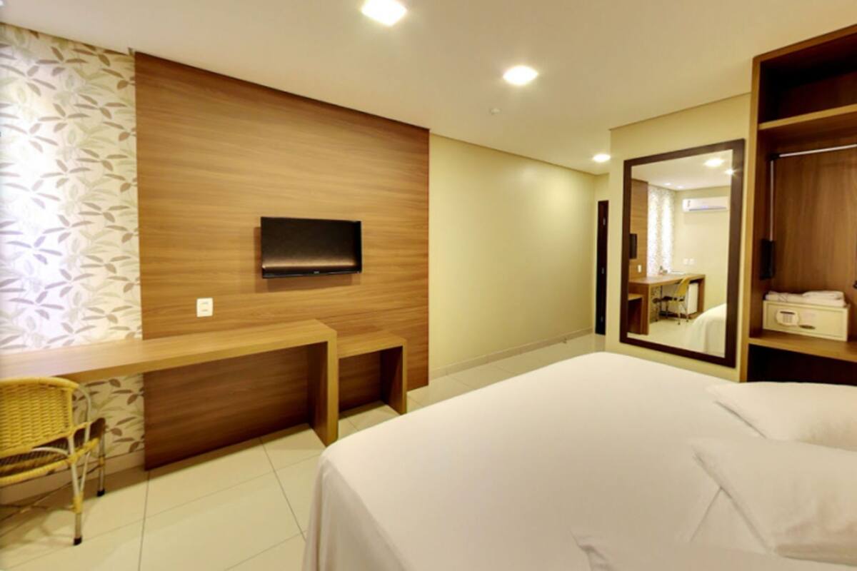 A hotel room with a bed, a desk, a chair, a TV, and a wardrobe.
