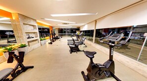 A modern gym with cardio machines, weight stations, and a large window offering a city view. - Hotel Taiamã (CUIABA)