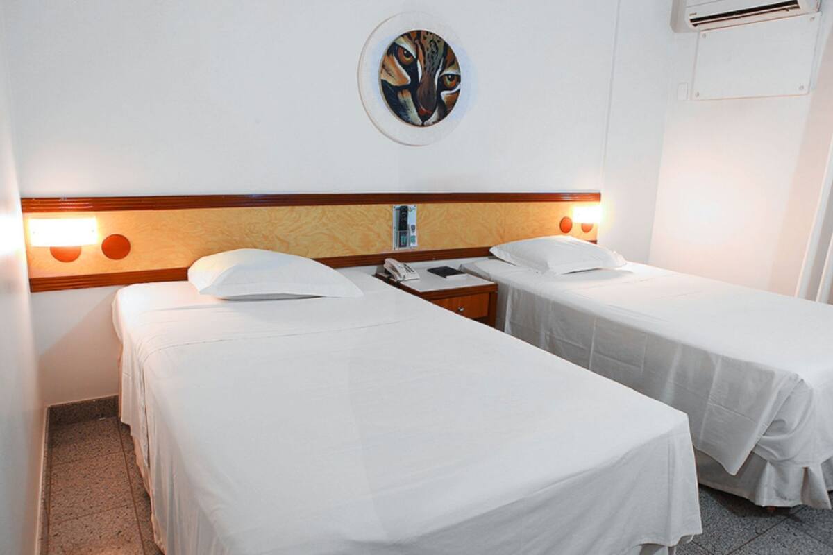 A hotel room with two single beds, a wooden headboard, a wall-mounted artwork, and a bedside table with a phone.