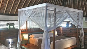 A four-poster canopy bed with white linens and a wooden frame, set against a backdrop of a thatched ceiling and a stone wall. - The Purist Villas & Spa (Ubud)