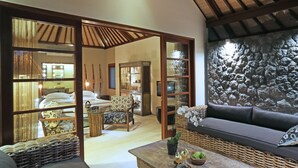 A room with a sofa, wicker furniture, a stone wall, and a wooden ceiling. - The Purist Villas & Spa (Ubud)