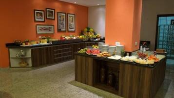 Un'area buffet con frutta e bevande assortite, un cartello con la scritta 'caffè' e quadri appesi alle pareti.
