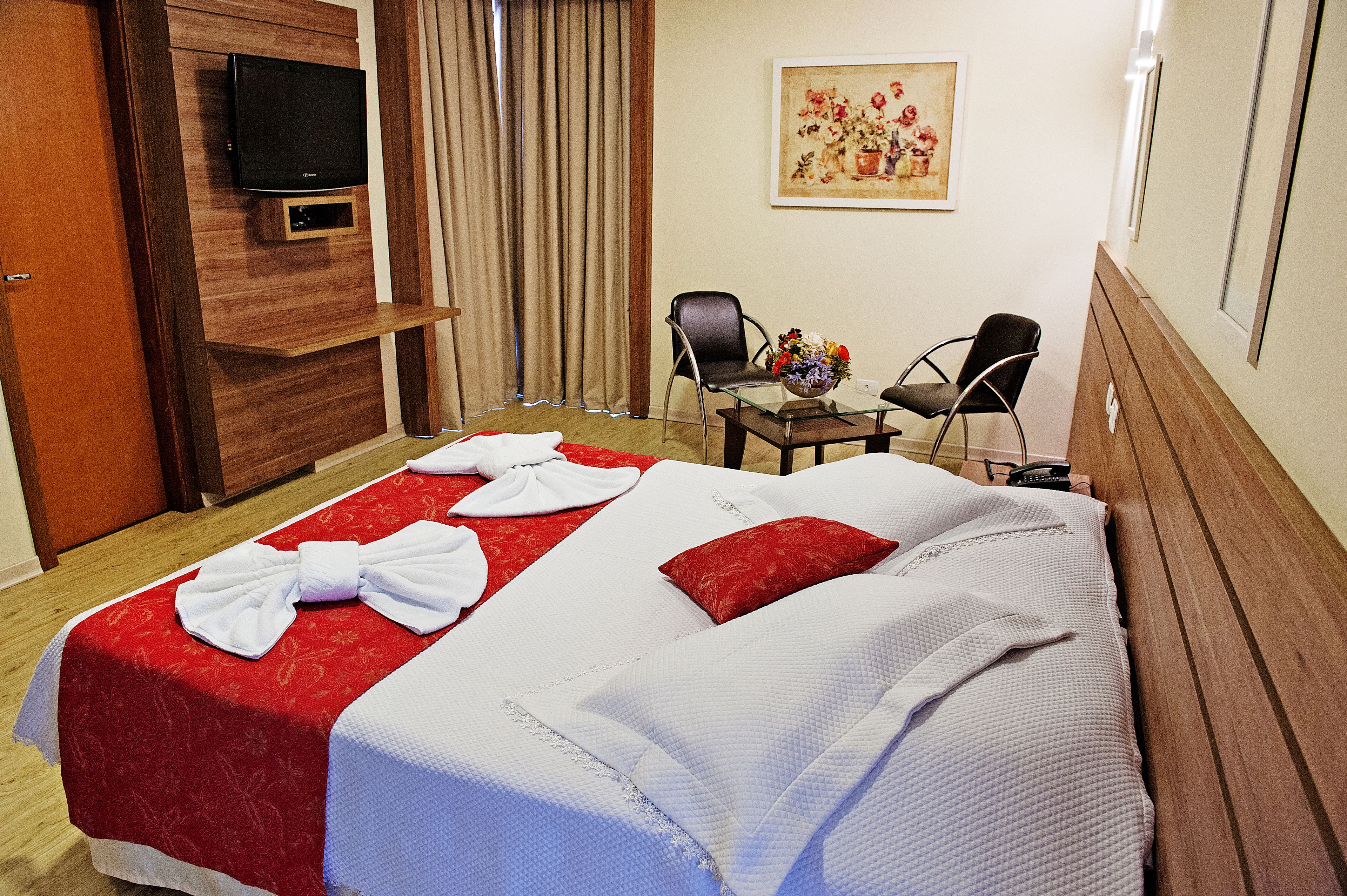 A hotel room with a bed, a TV, a desk with chairs, and a painting on the wall.