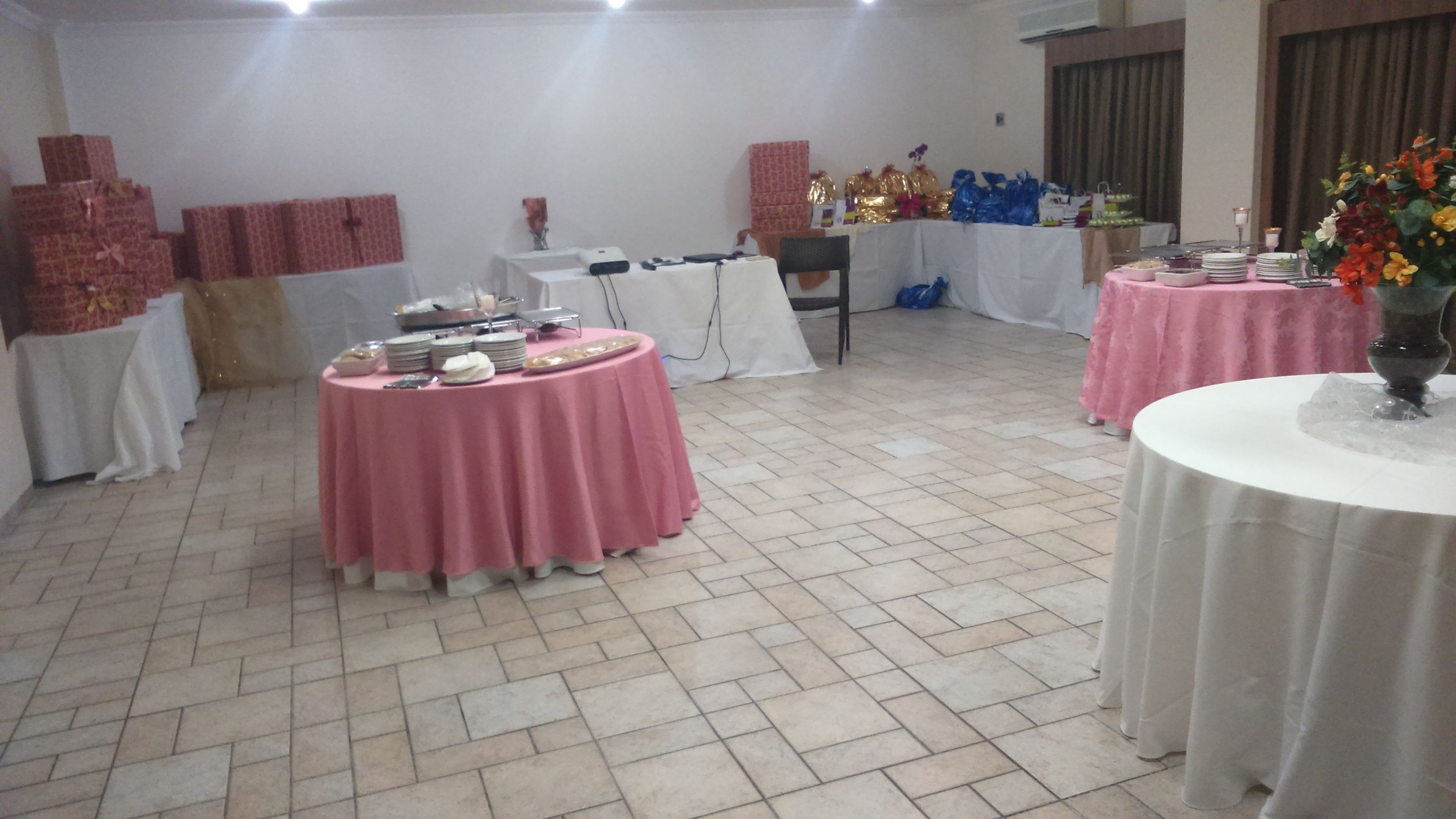A banquet hall with multiple round tables covered in pink and white tablecloths, arranged on a tiled floor.