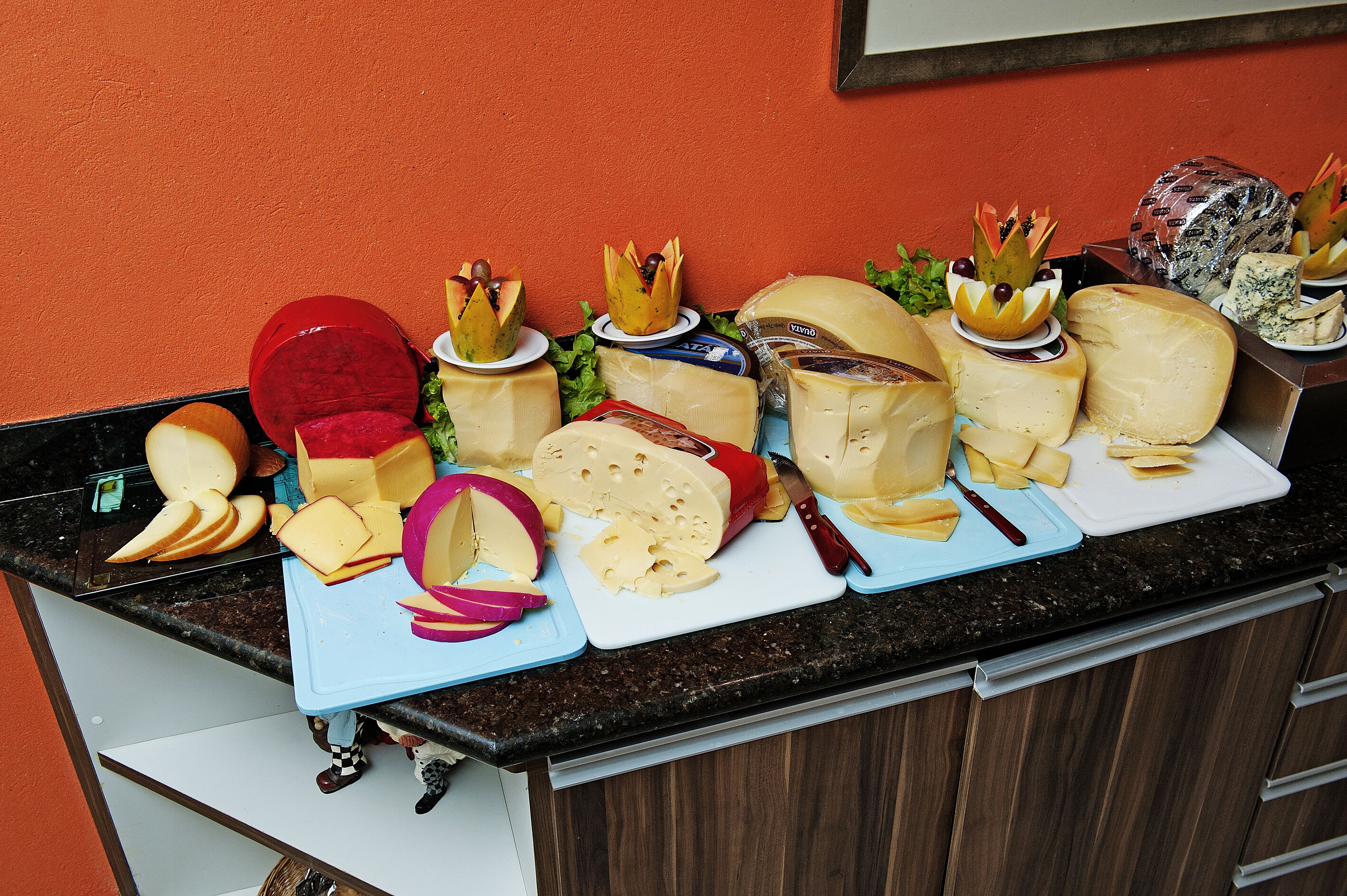 A variety of cheeses on a cutting board with a knife, set against an orange wall.
