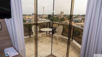 A balcony with a table and two chairs, a view of the cityscape, and a building with a red chimney.