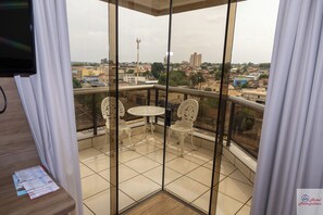 A balcony with a table and two chairs, a view of the cityscape, and a building with a red chimney. - Hotel Metropolitan (Campo Grande)