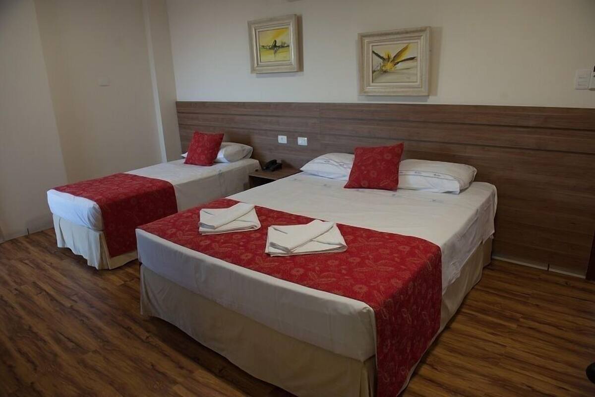 Two single beds with red bedding and white headboards in a room with wooden flooring.