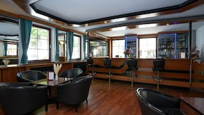A modern bar area with wooden flooring, black leather chairs, and a bar counter with a blue-lit shelf. - Hotel Sophienhof (Königs Wusterhausen)