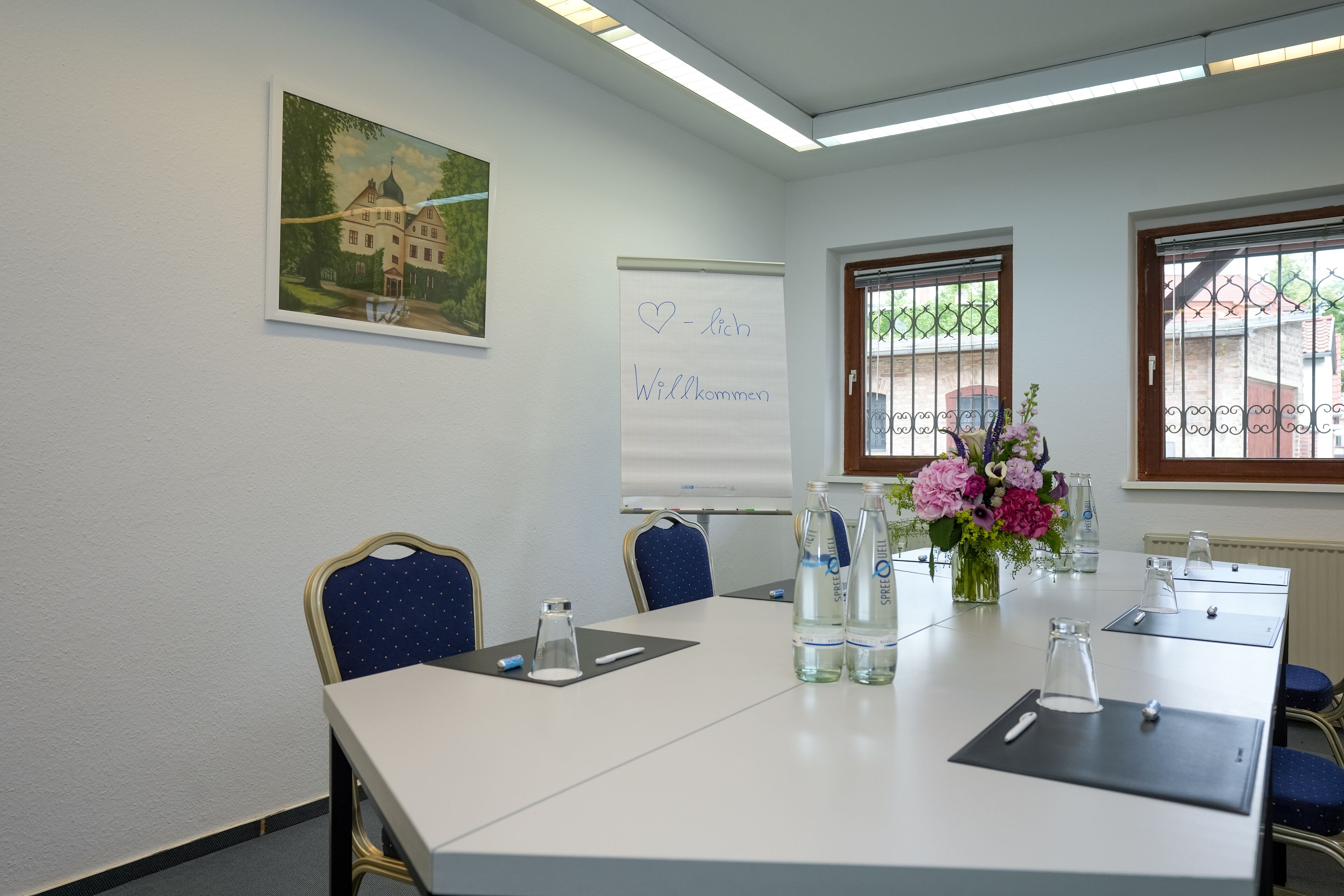 Ein Konferenzraum mit einer Wandtafel, einem Willkommensschild und einer Blumenkomposition.
