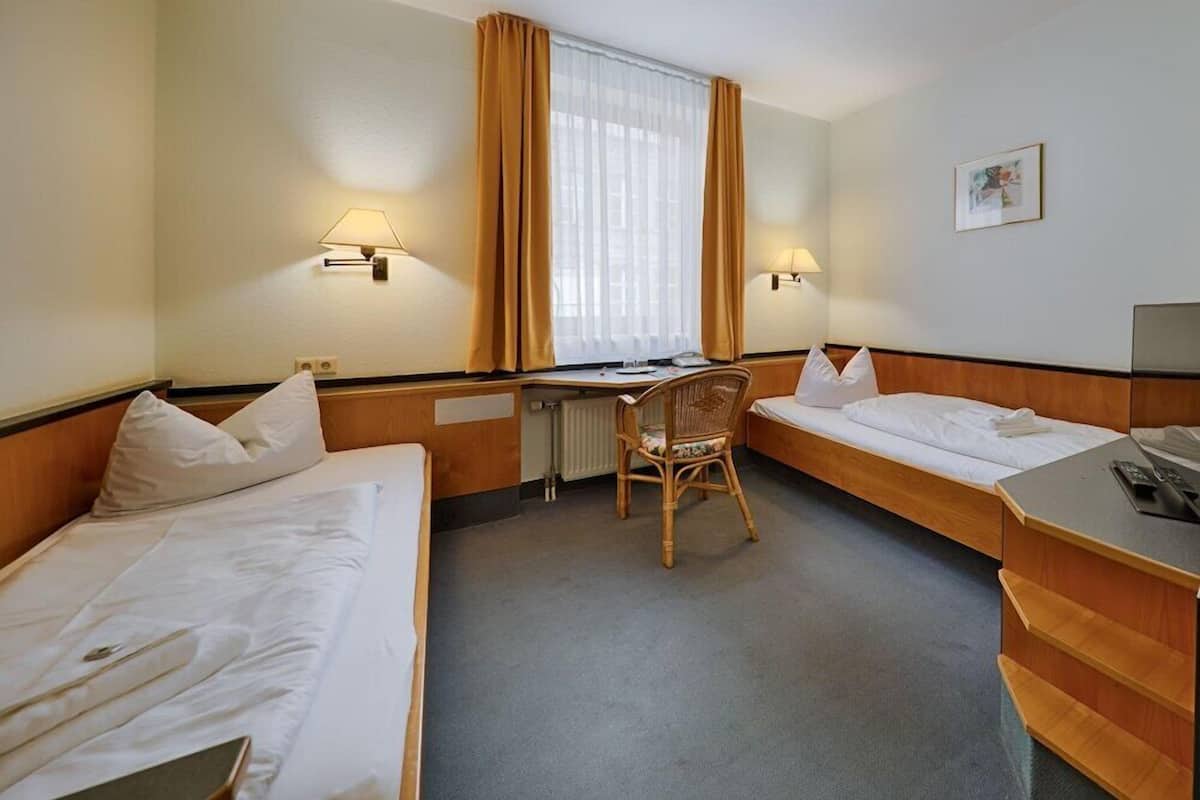 A hotel room with two beds, a desk, a chair, and a radiator.